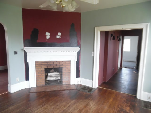 unfurnished living room featuring a brick fireplace, wood finished floors, baseboards, arched walkways, and a ceiling fan