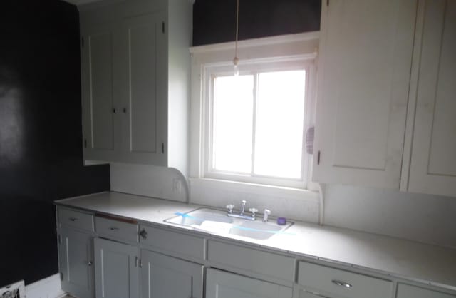 kitchen with a sink, white cabinetry, hanging light fixtures, and light countertops
