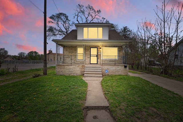 bungalow with covered porch, stone siding, fence, and a front yard