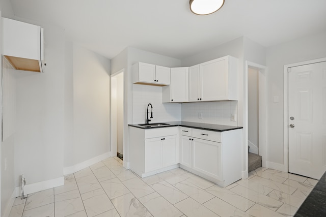 kitchen with dark countertops, a sink, marble finish floor, baseboards, and tasteful backsplash