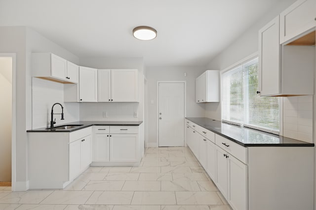 kitchen featuring white cabinets, dark countertops, a sink, marble finish floor, and decorative backsplash