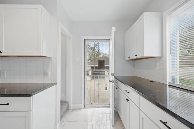 kitchen with decorative backsplash, baseboards, dark stone countertops, marble finish floor, and white cabinetry