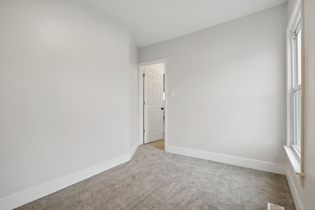 empty room with baseboards, visible vents, and light carpet