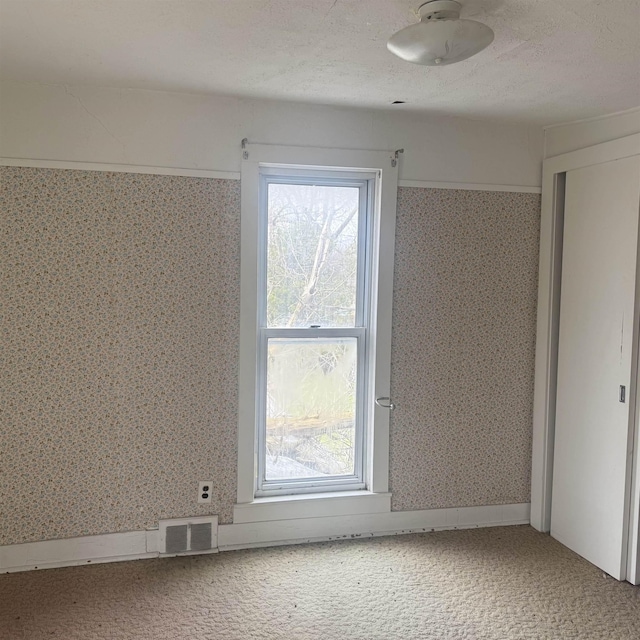 unfurnished room with visible vents, carpet, and wallpapered walls