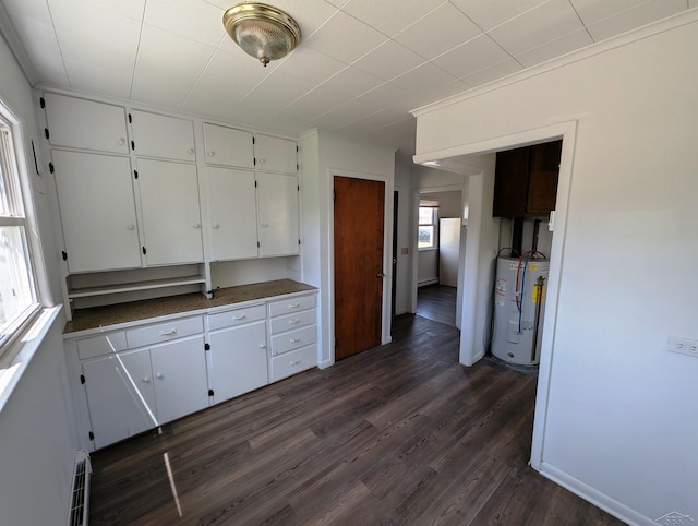 kitchen featuring dark countertops, dark wood finished floors, baseboards, water heater, and white cabinetry