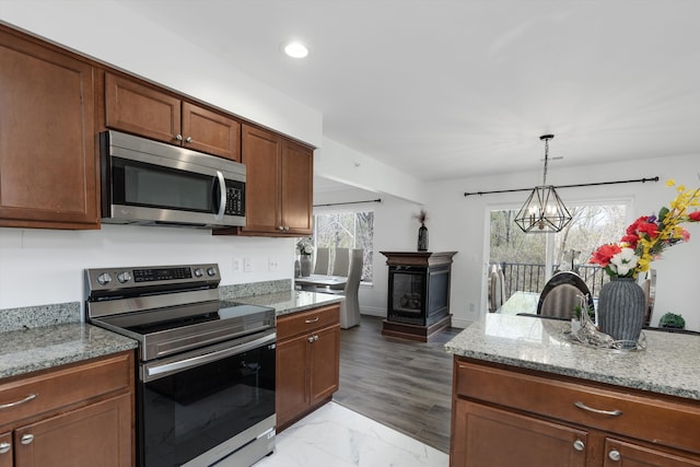 kitchen with light stone countertops, appliances with stainless steel finishes, an inviting chandelier, recessed lighting, and decorative light fixtures