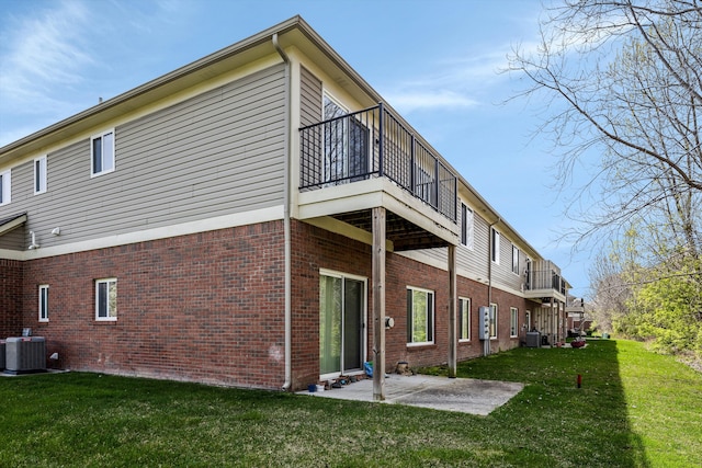rear view of house featuring a balcony, a patio, brick siding, central air condition unit, and a yard