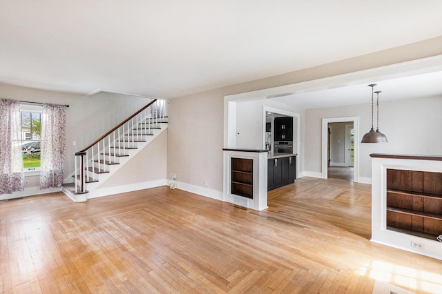 unfurnished living room featuring light wood-style floors, baseboards, and stairway