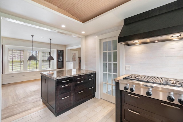 kitchen with light stone counters, hanging light fixtures, wall chimney exhaust hood, stainless steel gas stovetop, and wood ceiling