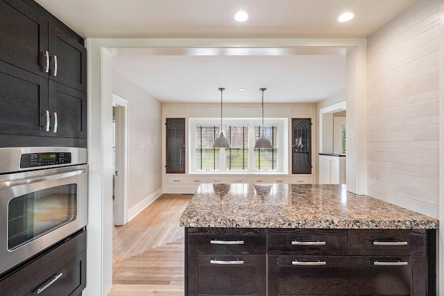 kitchen with light stone countertops, baseboards, stainless steel oven, light wood finished floors, and hanging light fixtures