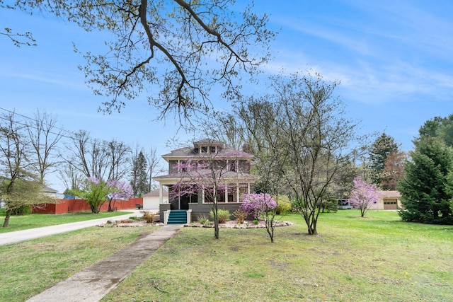 american foursquare style home with covered porch, fence, driveway, and a front lawn