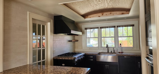 kitchen with lofted ceiling, wall chimney exhaust hood, tasteful backsplash, dark cabinets, and a sink