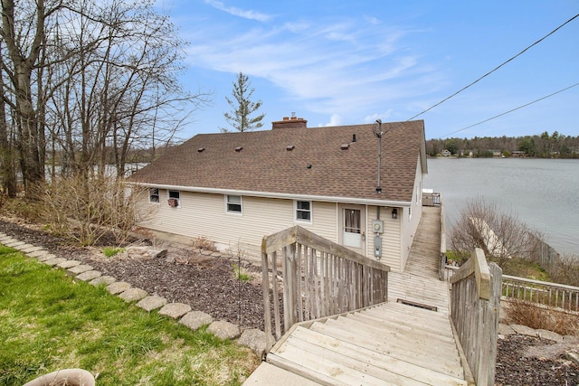 rear view of house with a chimney, a deck with water view, and roof with shingles