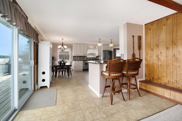 kitchen with appliances with stainless steel finishes, tasteful backsplash, a peninsula, a chandelier, and white cabinets