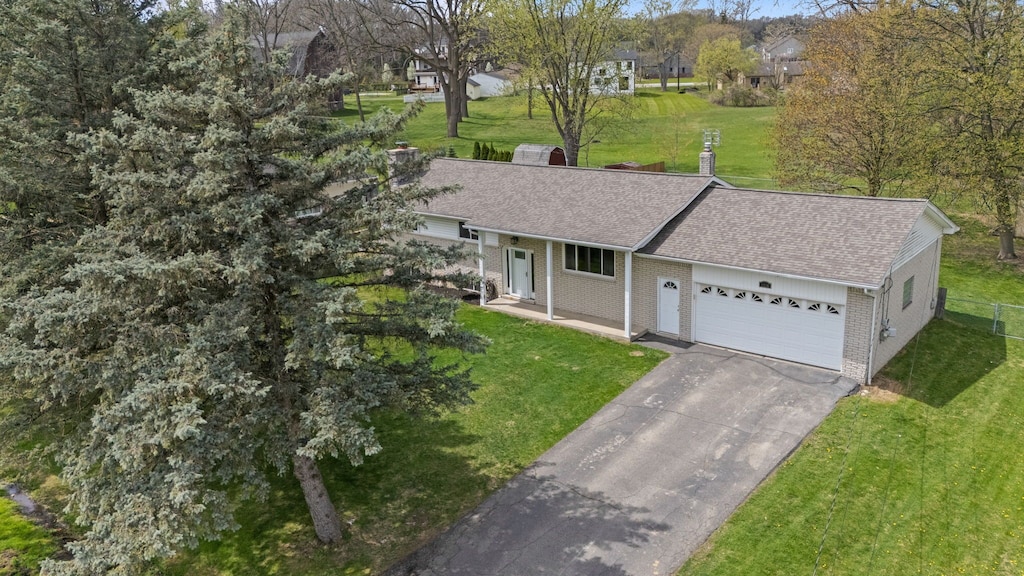 ranch-style house featuring a garage, a front yard, roof with shingles, brick siding, and driveway