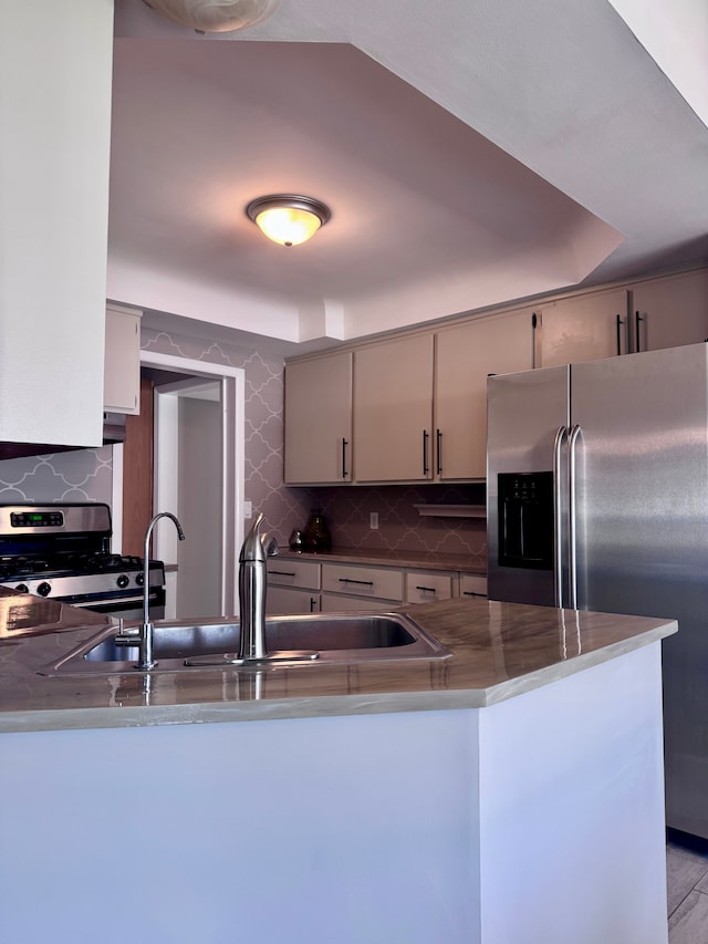 kitchen featuring a sink, appliances with stainless steel finishes, backsplash, and a peninsula