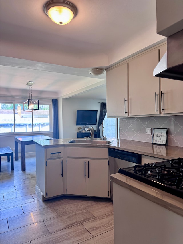 kitchen with wall chimney range hood, backsplash, dishwasher, a sink, and a peninsula