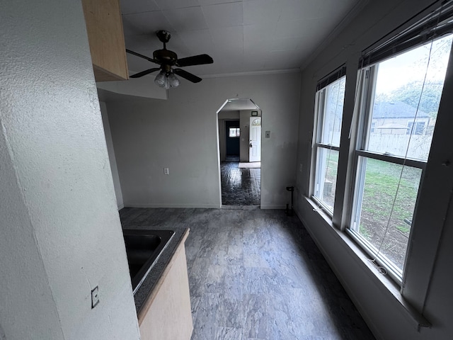 interior space featuring ceiling fan, arched walkways, wood finished floors, baseboards, and ornamental molding