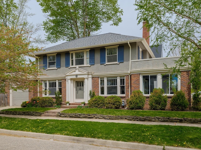 colonial-style house featuring a front lawn, brick siding, a garage, stucco siding, and a chimney