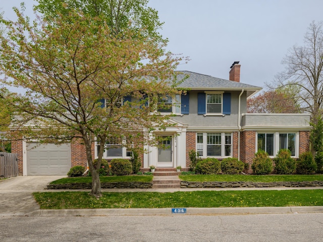 colonial inspired home featuring brick siding, a garage, a front yard, a chimney, and driveway