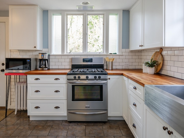 kitchen featuring stainless steel range with gas cooktop, radiator, wooden counters, and white cabinetry
