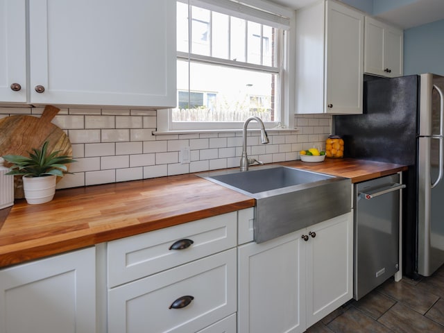 kitchen with appliances with stainless steel finishes, a sink, wood counters, white cabinetry, and backsplash