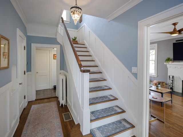 stairs with crown molding, wainscoting, a decorative wall, radiator, and wood finished floors