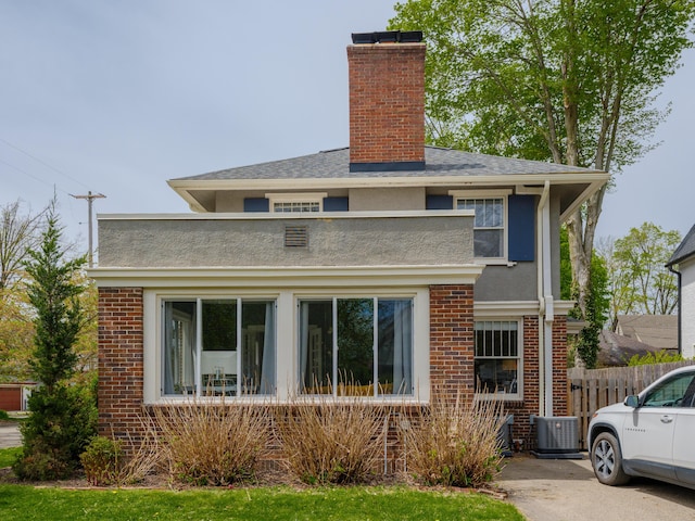 view of front facade featuring a chimney, brick siding, fence, cooling unit, and stucco siding