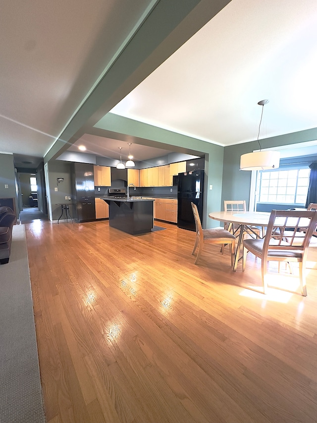 kitchen featuring pendant lighting, freestanding refrigerator, light wood finished floors, open floor plan, and an island with sink