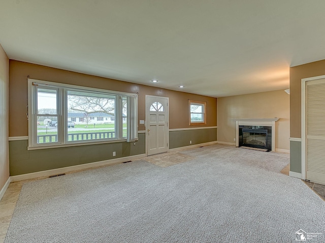 unfurnished living room featuring a fireplace with flush hearth, baseboards, light carpet, and visible vents