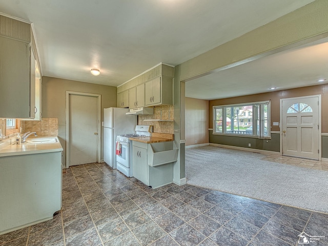 kitchen with decorative backsplash, a sink, baseboards, under cabinet range hood, and white appliances