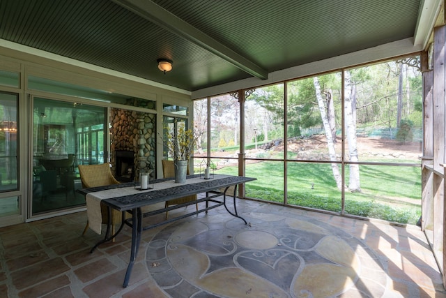 sunroom featuring a healthy amount of sunlight, a fireplace, and beam ceiling