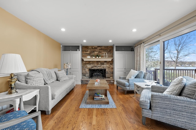 living room with recessed lighting, a stone fireplace, a water view, and light wood-type flooring