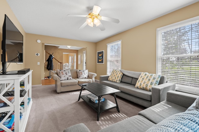 living area with baseboards, ceiling fan, light carpet, and stairway