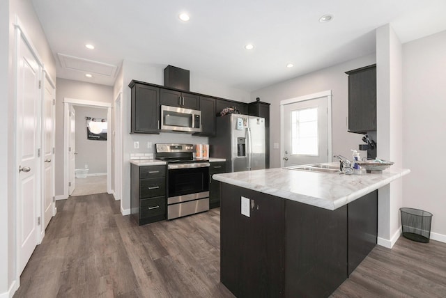 kitchen featuring appliances with stainless steel finishes, a sink, light countertops, a peninsula, and dark wood-style floors