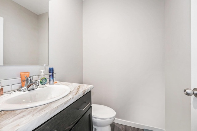 half bathroom featuring toilet, baseboards, wood finished floors, and vanity