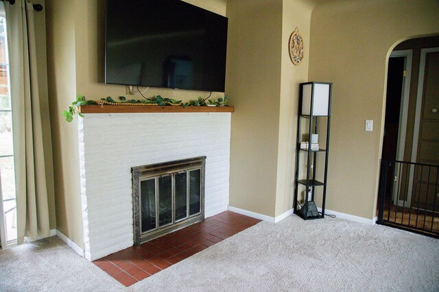unfurnished living room with baseboards, carpet flooring, arched walkways, and a fireplace