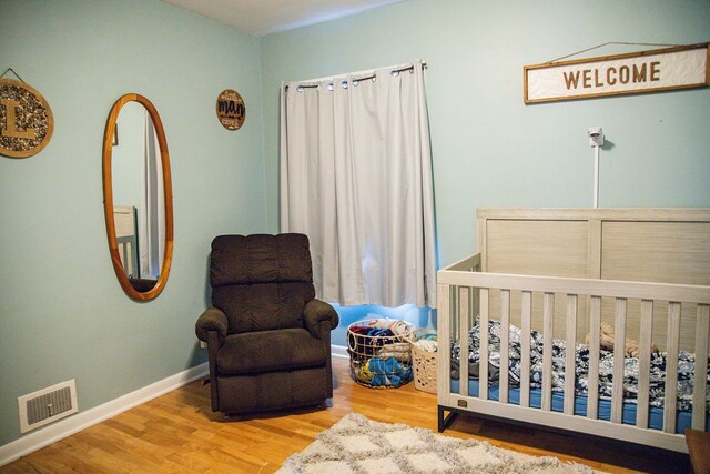 bedroom featuring visible vents, baseboards, a crib, and wood finished floors