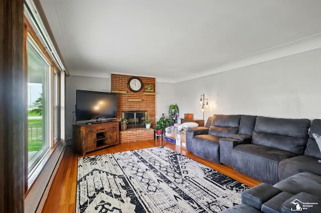 living room featuring crown molding, a baseboard heating unit, wood finished floors, and a fireplace