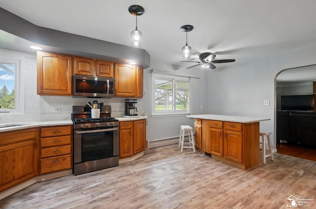 kitchen with backsplash, a kitchen bar, appliances with stainless steel finishes, light countertops, and light wood-style flooring