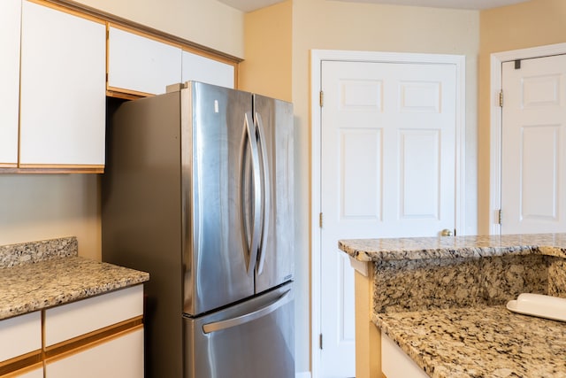 kitchen featuring freestanding refrigerator, white cabinets, and light stone counters