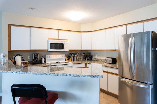 kitchen featuring light stone counters, white cabinetry, a peninsula, and white appliances