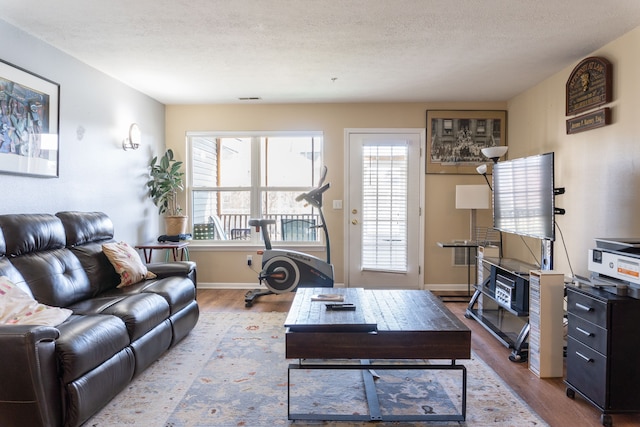 living area with a textured ceiling, baseboards, wood finished floors, and visible vents