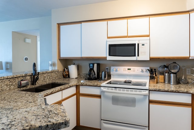 kitchen with light stone counters, a sink, white cabinetry, and white appliances