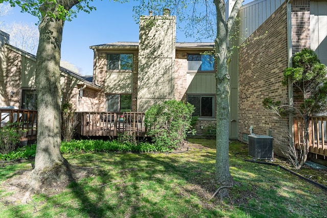 back of house featuring brick siding, a deck, central AC unit, a chimney, and a yard