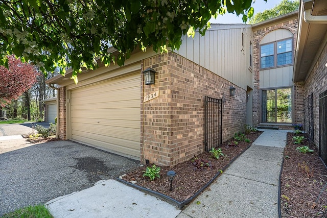 view of side of property featuring an attached garage, aphalt driveway, and brick siding