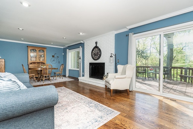 living room featuring crown molding, a fireplace, wood finished floors, and visible vents