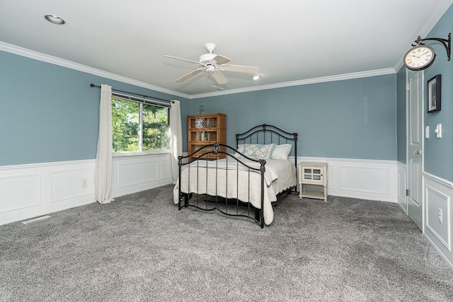 carpeted bedroom with crown molding, a ceiling fan, wainscoting, and a decorative wall