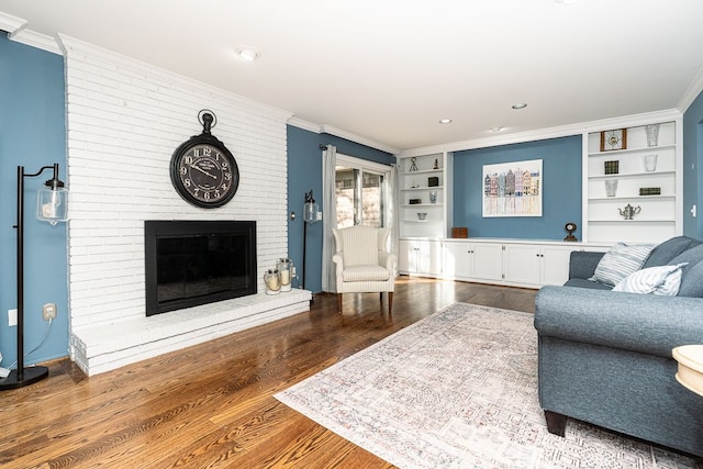 living area with ornamental molding, built in features, wood finished floors, and a fireplace