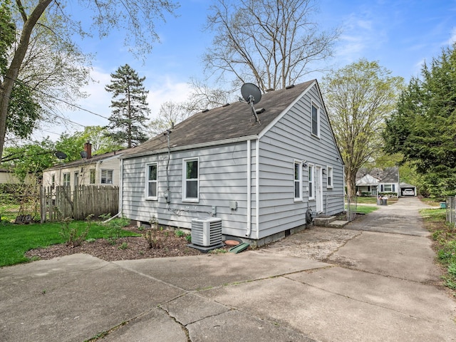view of side of home with central AC unit, fence, driveway, and a shingled roof